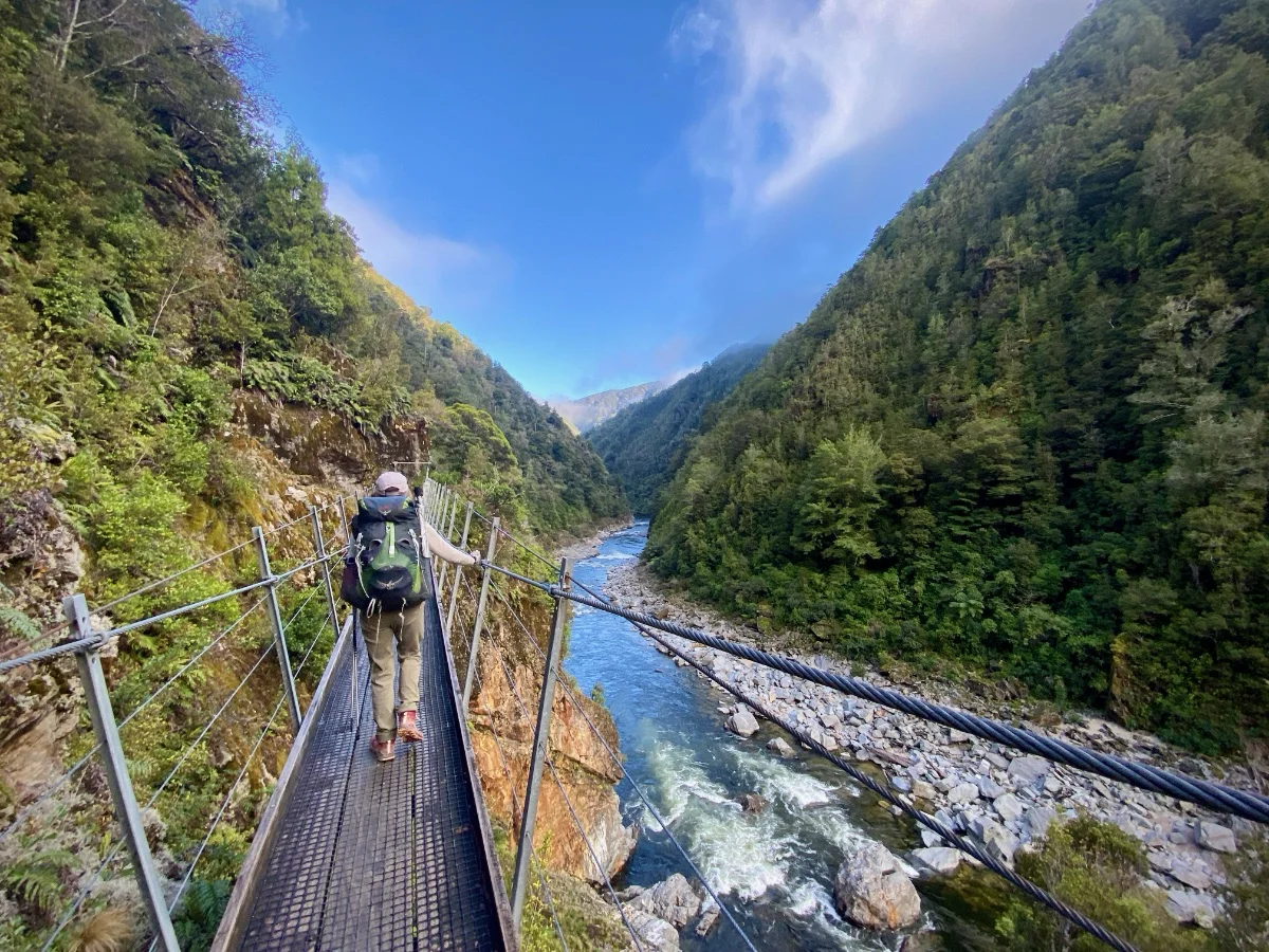 Tramper crossing a swing bridge in the Mokihinui River gorge on The Old Ghost Road